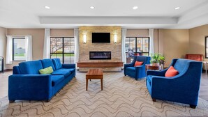 A spacious living room with a stone fireplace, blue sofas, and a flat-screen TV. - Comfort Inn & Suites West - Medical Center (Rochester)
