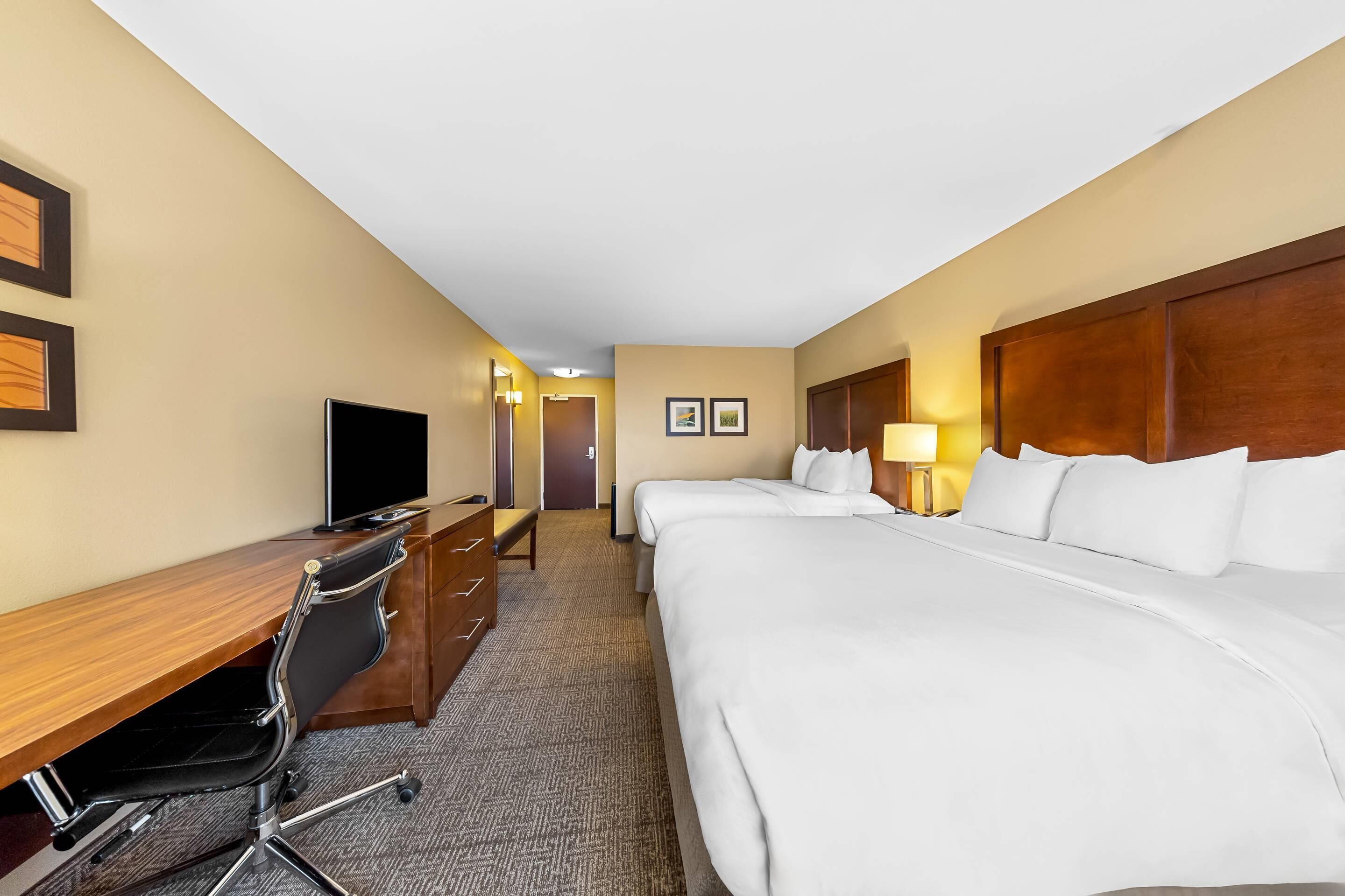 A hotel room with a desk, two beds, a chair, and a TV.