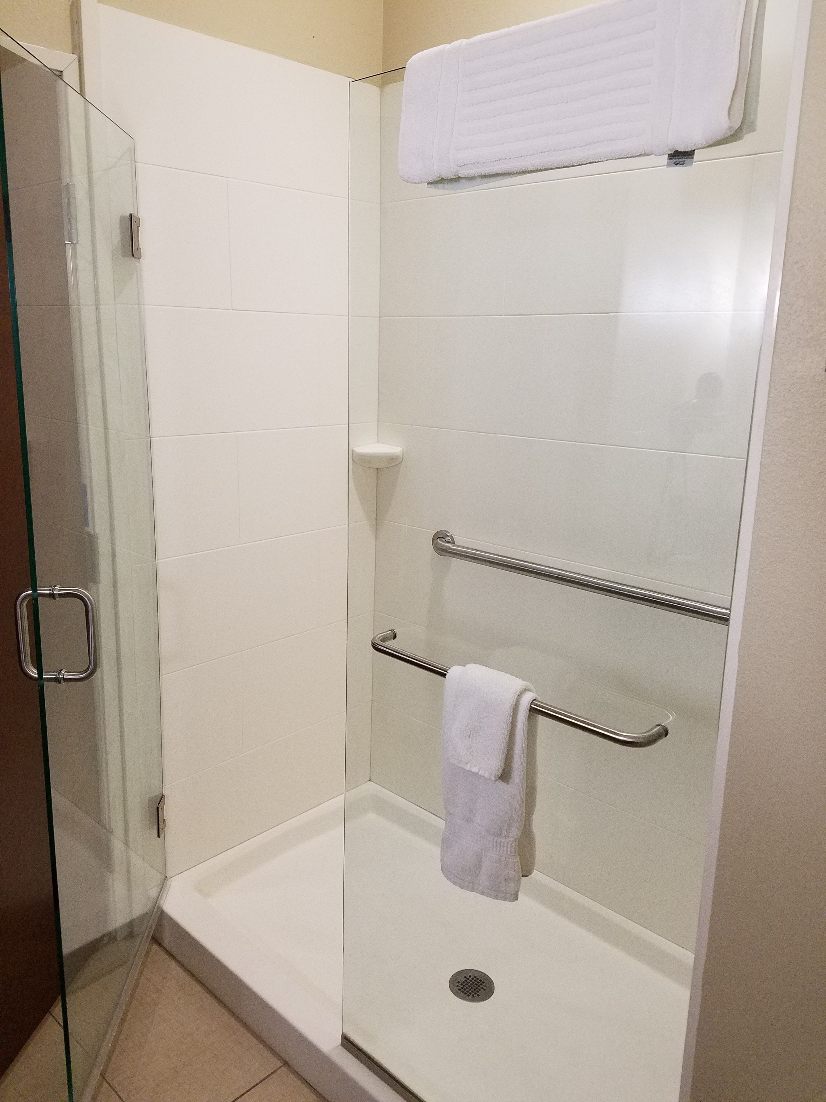 Douchecabine met glazen wanden, witte betegelde muur, glazen deur en metalen handgreep.
