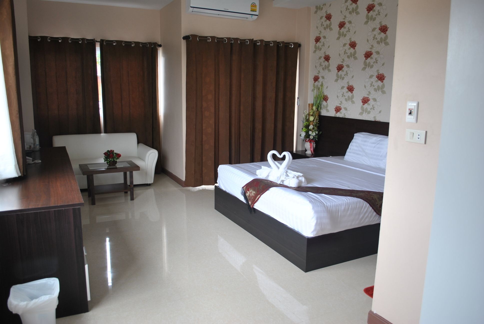 A hotel room with a bed, a sofa, a small table, and a trash bin.