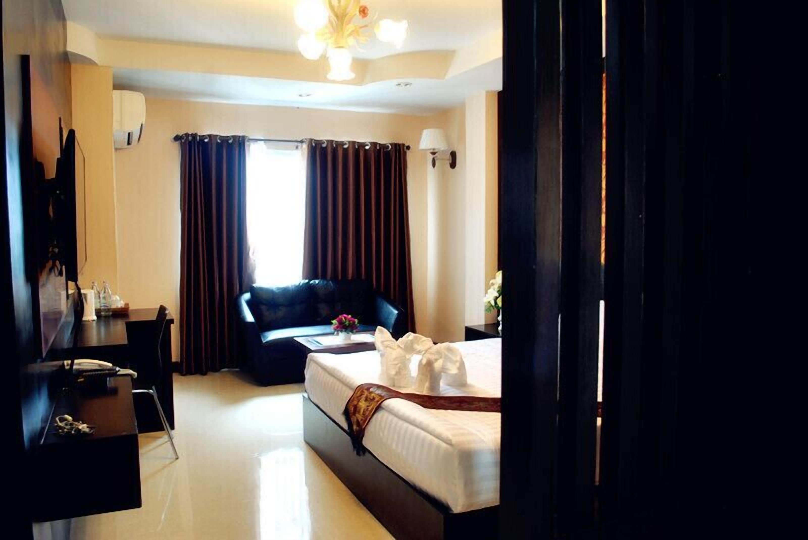 A hotel room with a bed, a desk, a chair, a sofa, and a window with curtains.