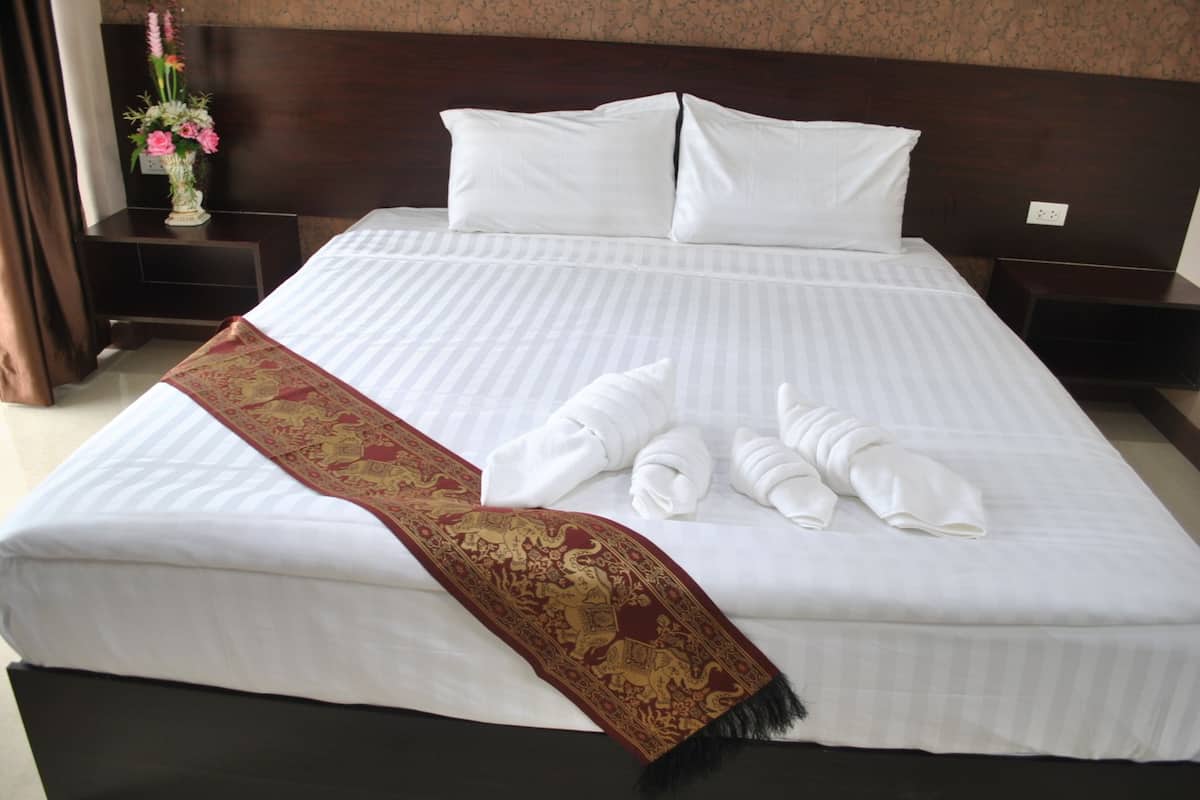 A neatly made bed with white linens, a red and gold decorative throw, and towels folded on the bed.