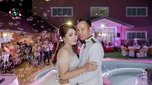 A couple embracing at a wedding reception with guests in the background. - Le Parc Wangnang (Phitsanulok)