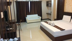 A hotel room with a large bed, a white sofa, a TV, and a dining area with plates and glasses. - Le Parc Wangnang (Phitsanulok)