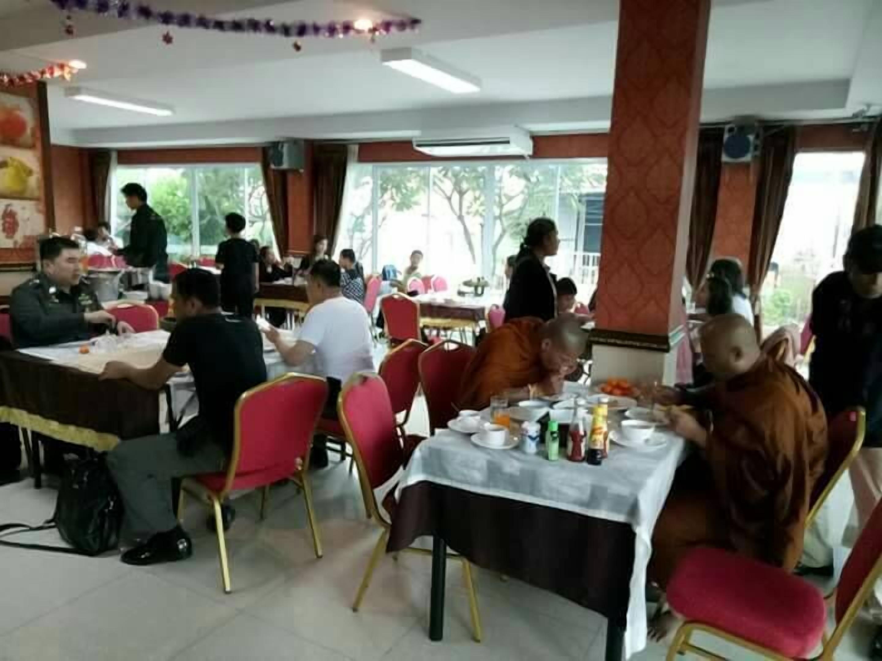 A dining area with tables and chairs, people seated and eating, and a view of the outdoors through large windows.