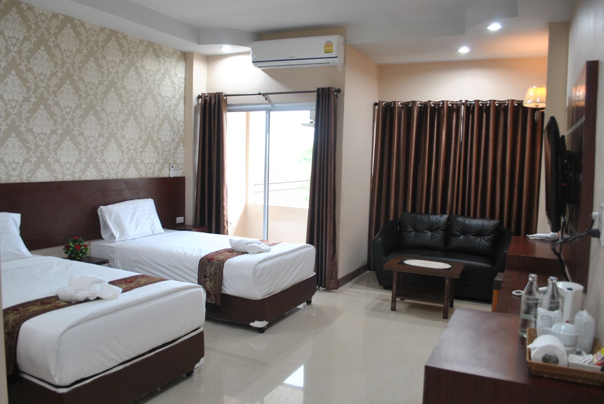 A hotel room with two beds, a sofa, a small table, and a TV.