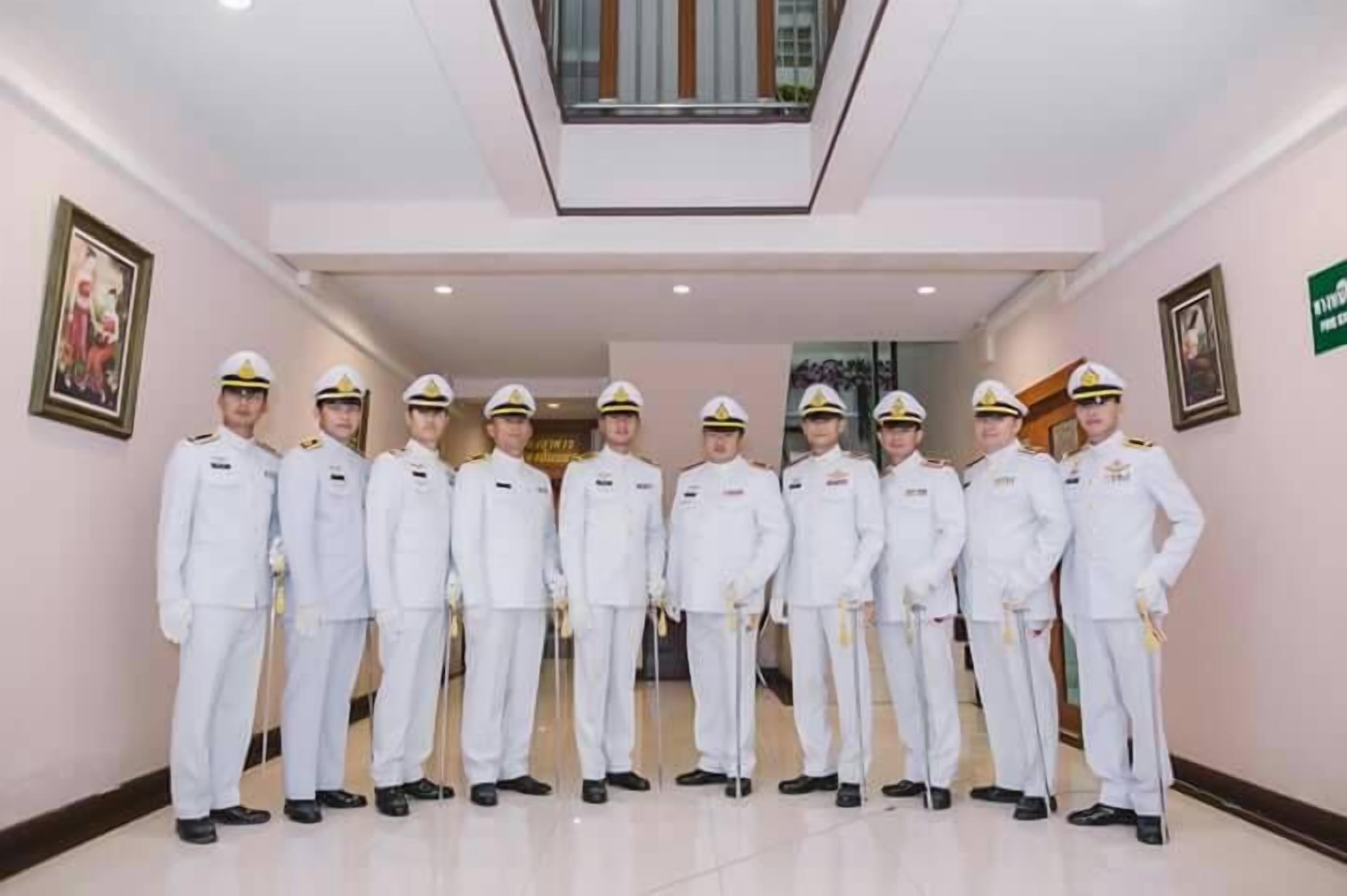 A group of uniformed personnel standing in a hallway with a ceiling light fixture and framed artwork on the walls.