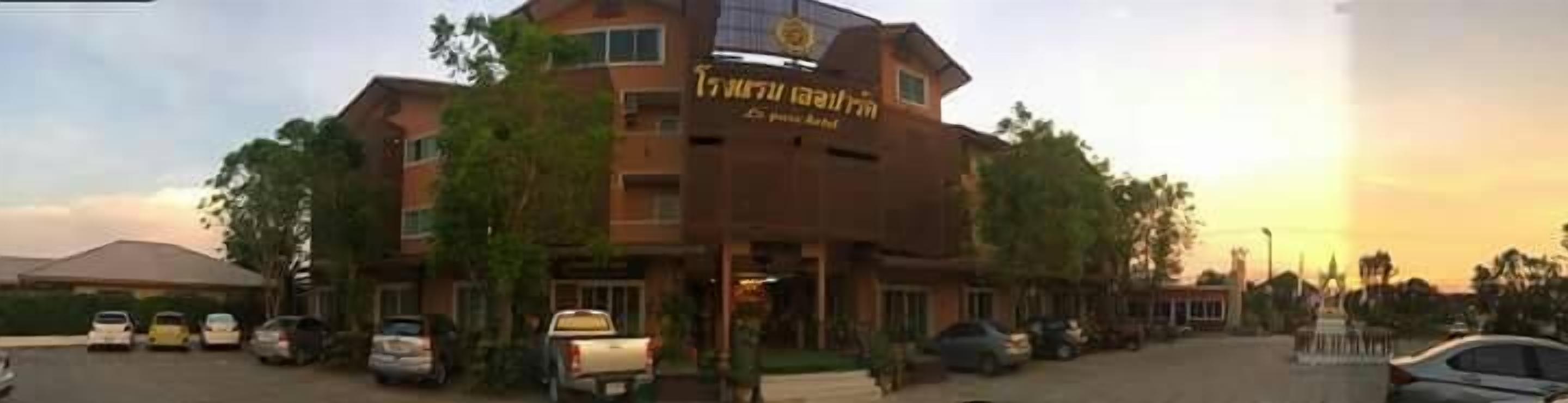 A multi-story building with a sign indicating it is a hotel. There are several cars parked in front, and the building has a flat roof.