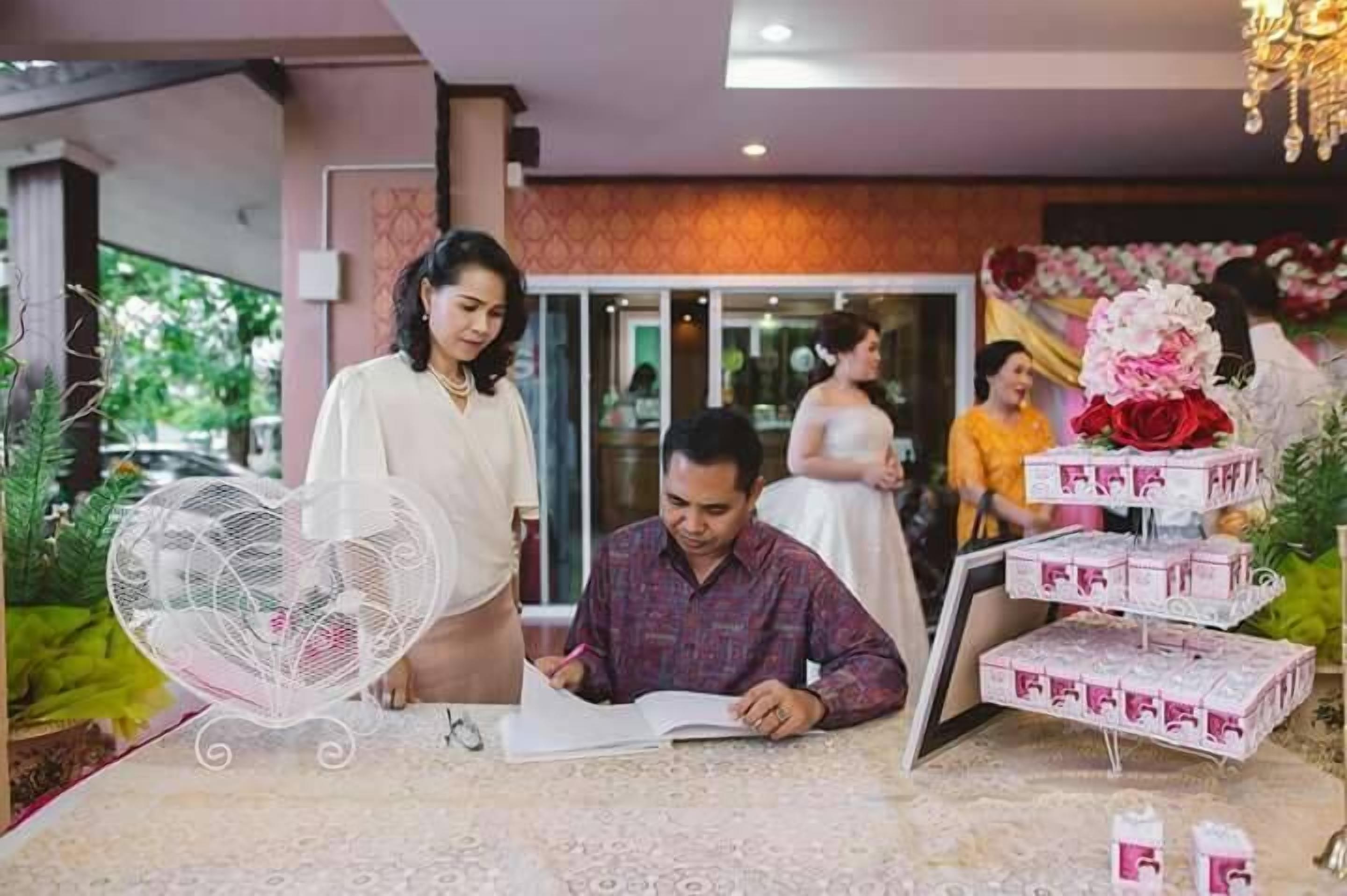 A man signing a document at a table with a decorative fan and a tiered box display.