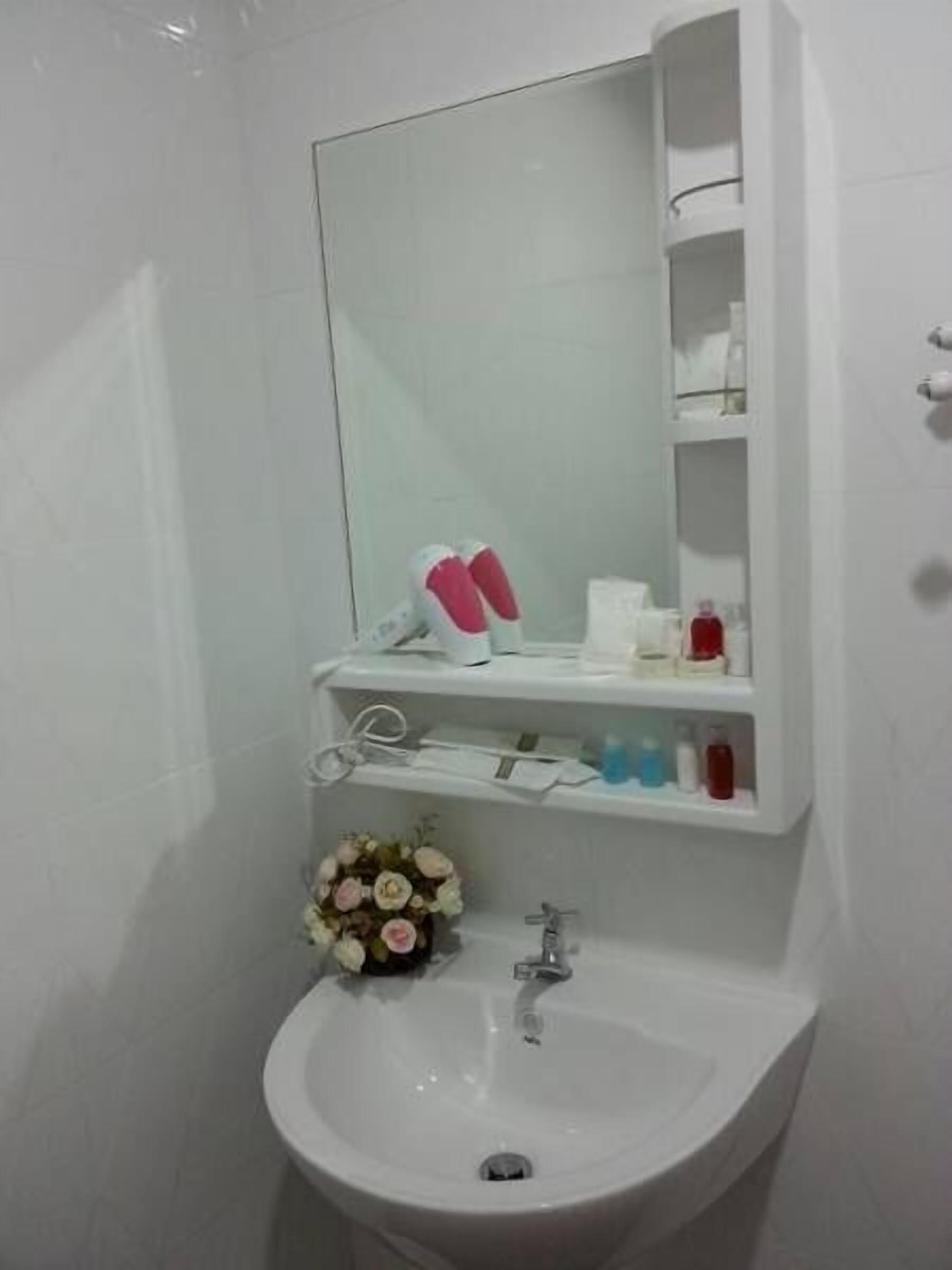 A bathroom with a white sink, mirror, and shelves with toiletries.