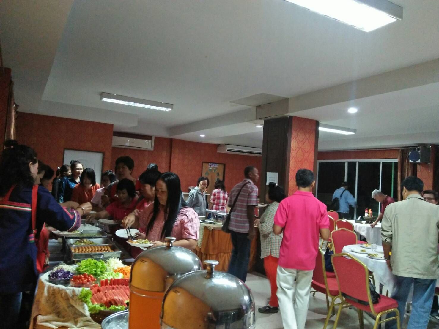 A buffet setup with various food items and people serving and eating.