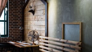 Una habitación rústica con vigas de madera a la vista, pared de ladrillo, cabeza de venado montada en la pared, un ventilador y un banco de madera.