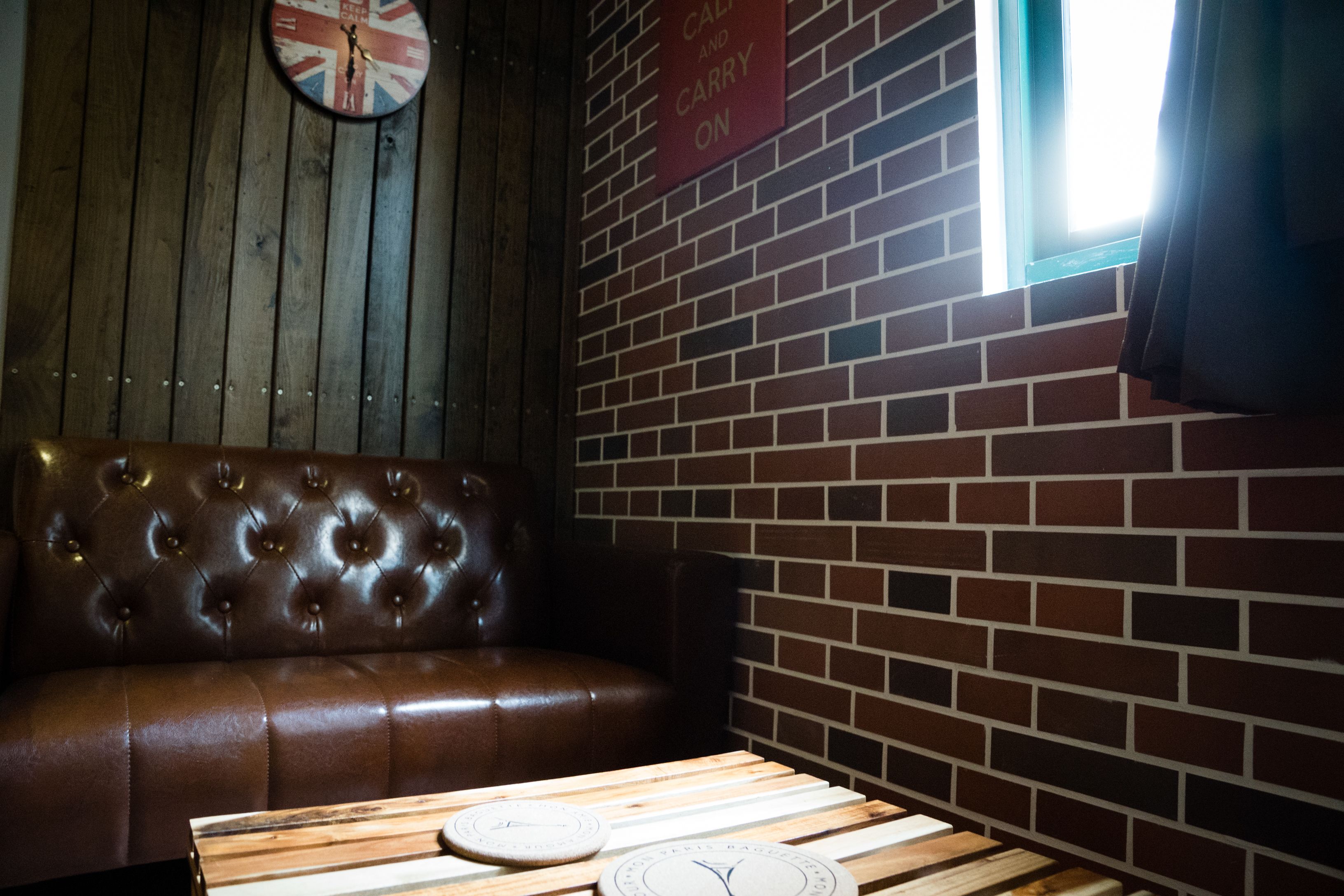 A wooden bench and a table with clocks, a brick wall, and a window with curtains.
