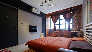 Un dormitorio moderno con una cama grande, un televisor de pantalla plana, una ventana con cortinas y una pared de ladrillo.