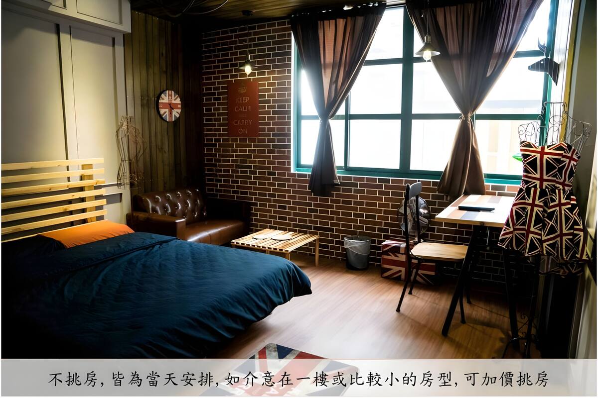 A compact hotel room with a bed, a small seating area, a table, and a window with curtains.