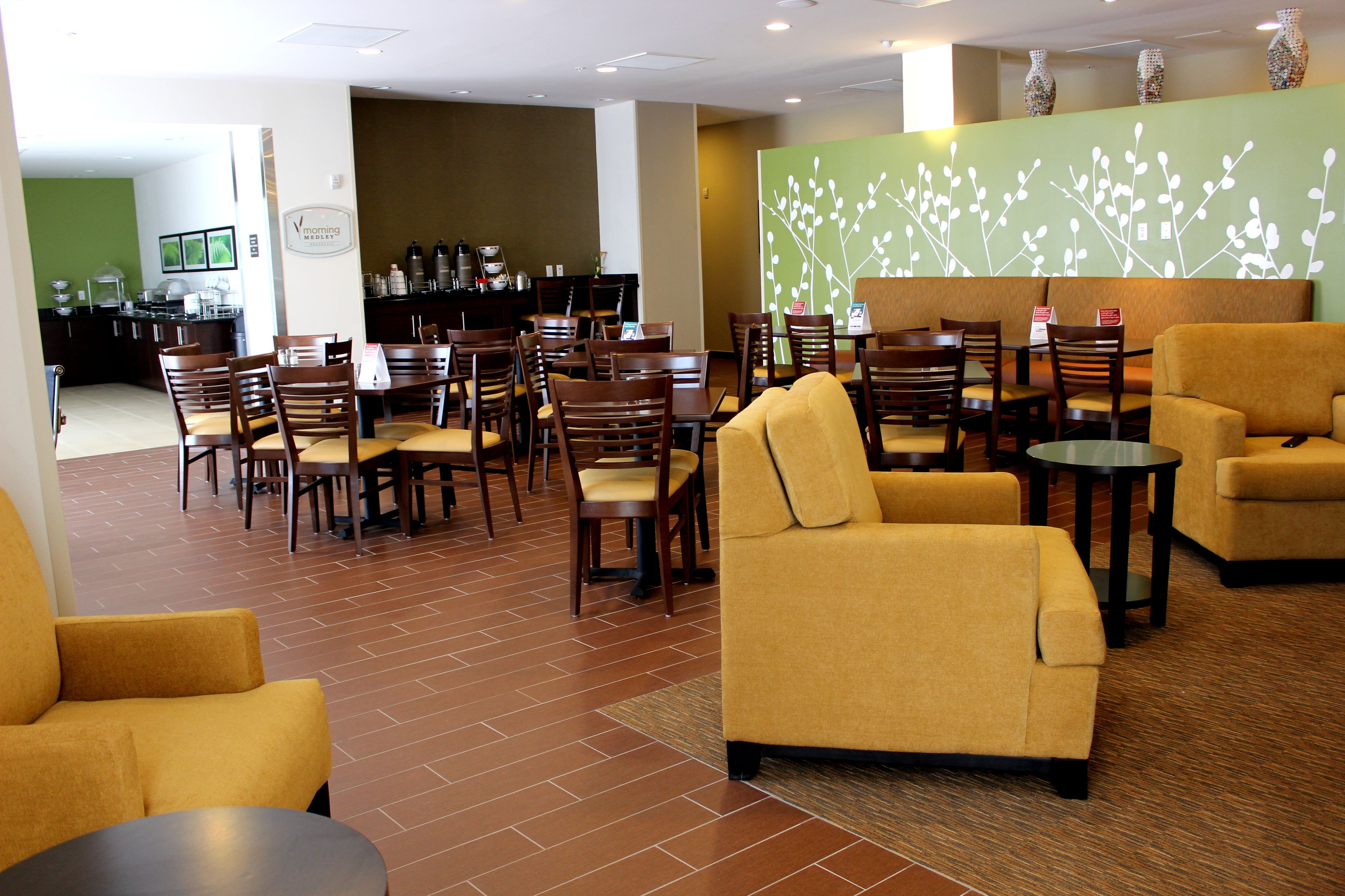 Un vestíbulo de hotel con varias zonas de estar, incluyendo sofás y sillones, una estación de café y un mostrador de recepción.