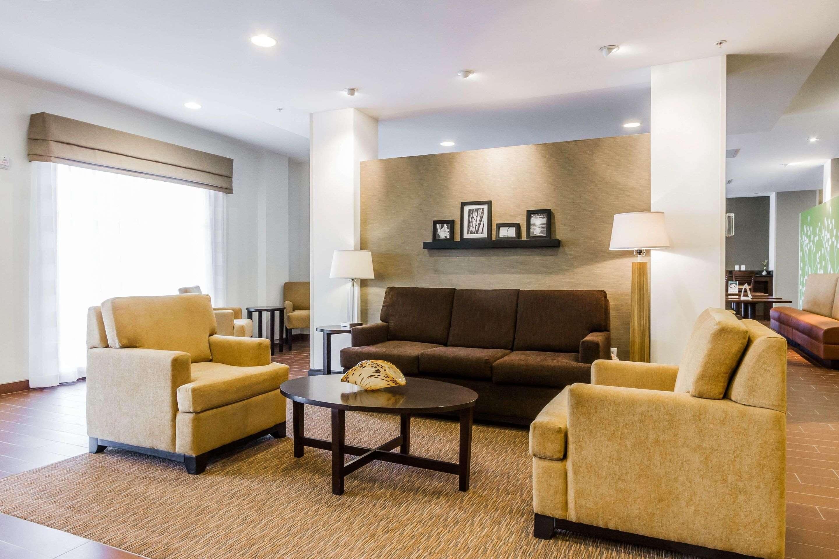 Un vestíbulo moderno de hotel con un sofá marrón, dos sillones, una mesa de centro y una lámpara.