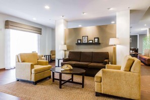 A modern hotel lobby with a brown sofa, two armchairs, a coffee table, and a lamp.