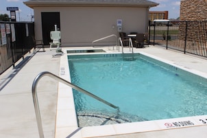 Una piscina con un cartel de prohibido bucear, una baranda de metal y una silla.