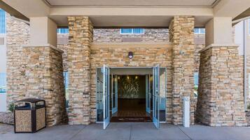 A building entrance with stone walls, a welcome mat, and a trash bin.