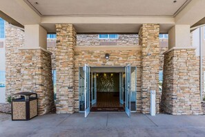 A building entrance with stone walls, a welcome mat, and a trash bin. - Spark by Hilton Odessa (Odessa)