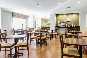 A restaurant with multiple tables and chairs, a counter with a coffee machine, and a wall-mounted sign. - Spark by Hilton Odessa (Odessa)
