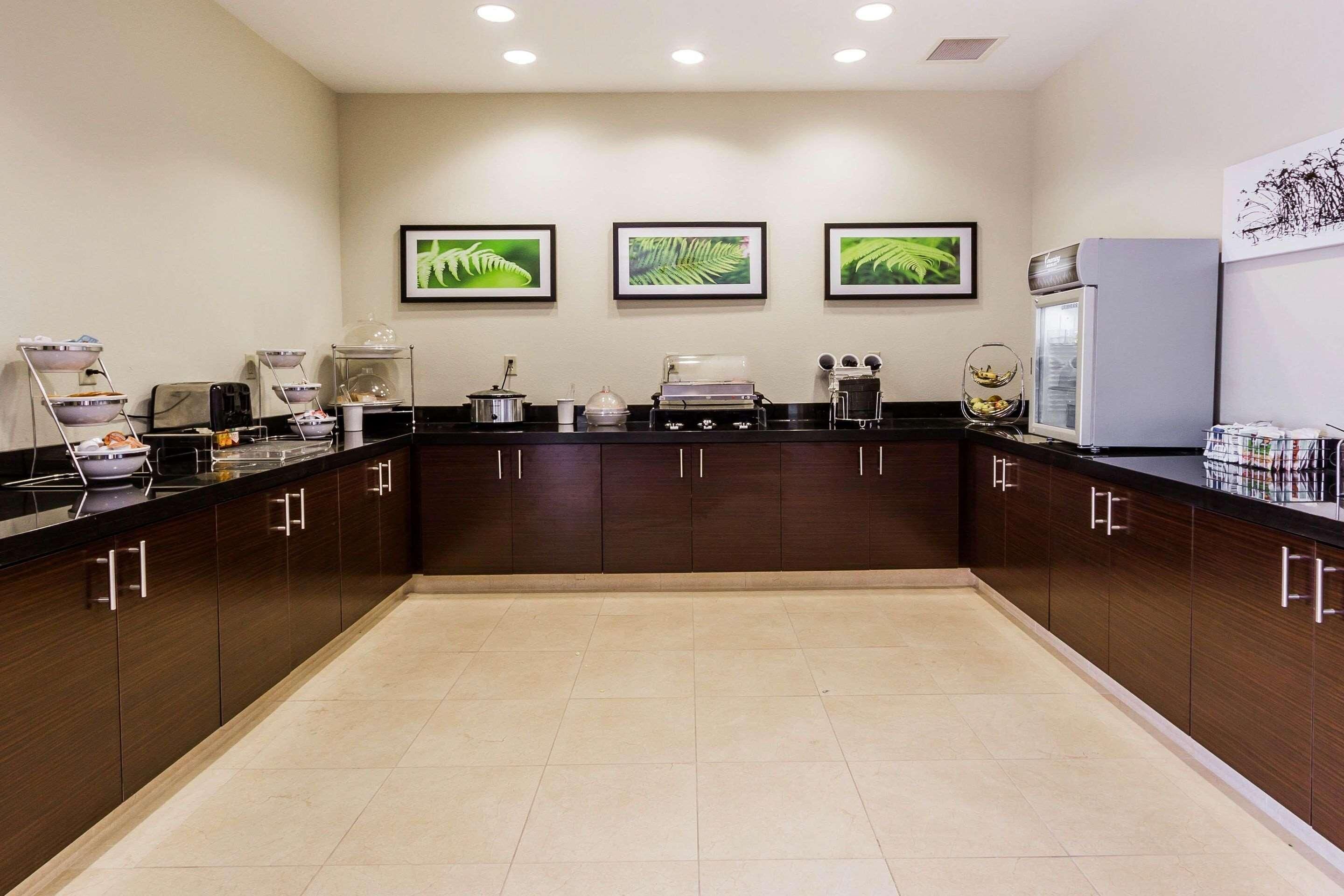 A modern kitchen with dark wooden cabinets, a black countertop, and three framed leaf artworks on the wall.