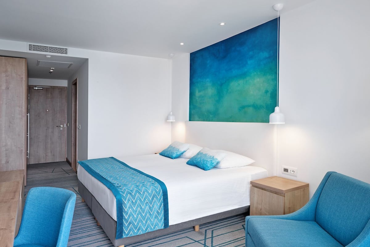 Ein modernes Hotelzimmer mit einem großen Bett, zwei Nachttischen, einem Schreibtisch und einem Sessel.