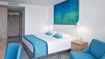 Een moderne hotelkamer met een groot bed, twee blauwe stoelen, een klein houten bijzettafeltje en een groot abstract schilderij aan de muur.