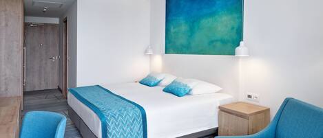 Et moderne hotelværelse med en stor seng, to blå stole, et lille træbord og et stort abstrakt billede på væggen.