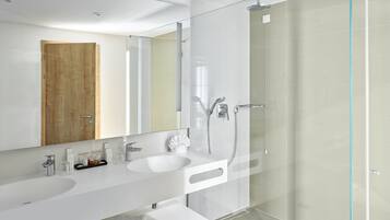 Un baño moderno con un espejo grande, dos lavamanos, una cabina de ducha de vidrio y una puerta de madera.