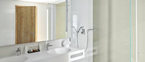 Un baño moderno con un espejo grande, dos lavamanos, una cabina de ducha de vidrio y una puerta de madera.