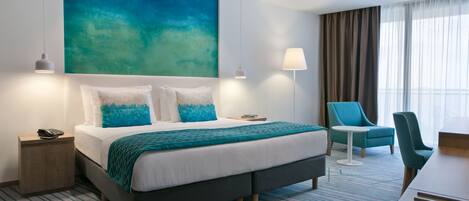 Habitación de hotel moderna con una cama grande, un escritorio, una silla y vistas al exterior.