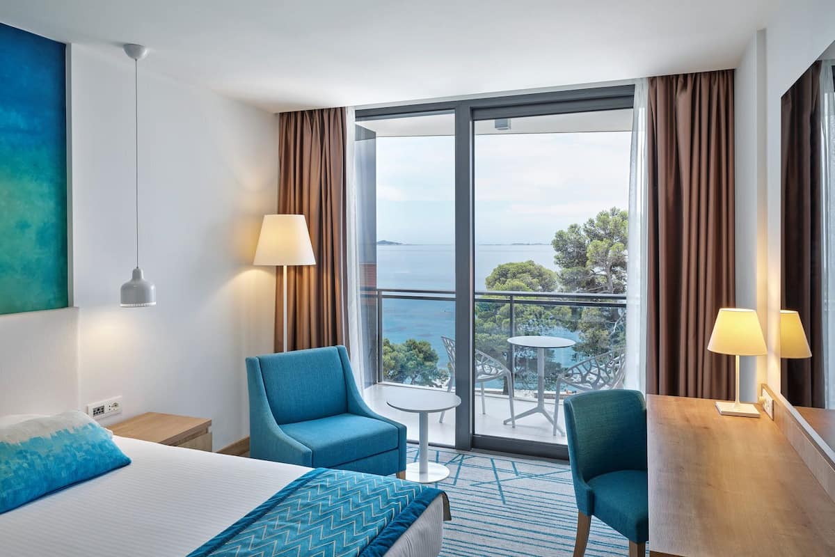 Ein Hotelzimmer mit Bett, zwei Stühlen, einem kleinen Tisch und einem Balkon mit Meerblick.