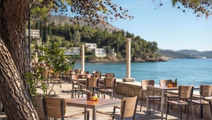 An outdoor cafe with tables and chairs, overlooking a body of water and hills.