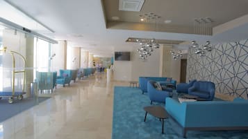 A modern lobby with a blue sofa set, a glass elevator, and a geometric wall design.