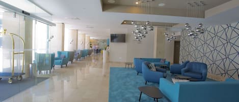 Een moderne lobby met een blauwe zithoek, een glazen lift en een wand met geometrische patronen.