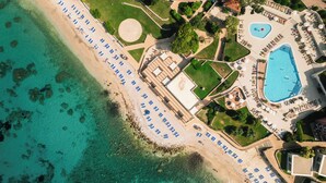 An aerial view of a resort with a beach, a swimming pool, and a large building with a flat roof.