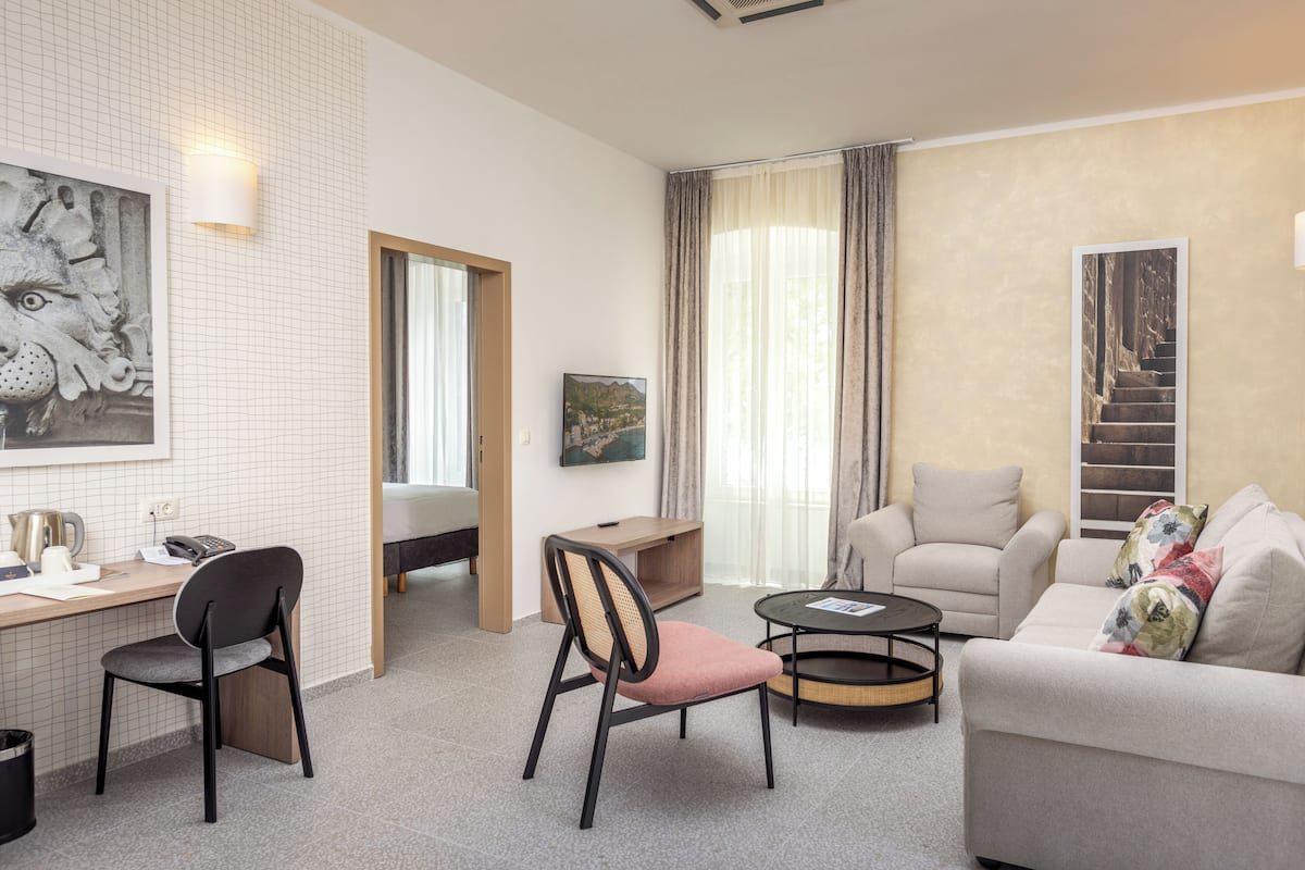 Ein modernes Hotelzimmer mit Schreibtisch, zwei Stühlen, einer Couch, einem Couchtisch und Kunstwerken an den Wänden.