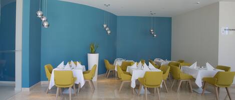 Un comedor con mesas y sillas, una planta en maceta y lámparas colgantes.
