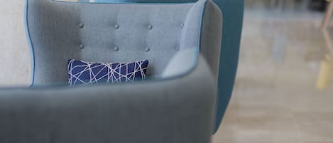 A modern lounge area with sofas and chairs, a glass partition, and a geometric wall design.