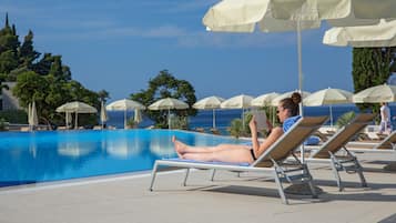 A poolside area with lounge chairs and umbrellas, a clear blue sky, and a view of the sea.
