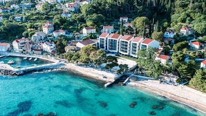 Vue aérienne d’une ville côtière avec un port de plaisance, des bâtiments aux toits rouges et des eaux turquoise cristallines.