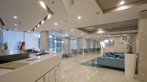 A modern hotel lobby with a reception desk, seating area, and a television screen.