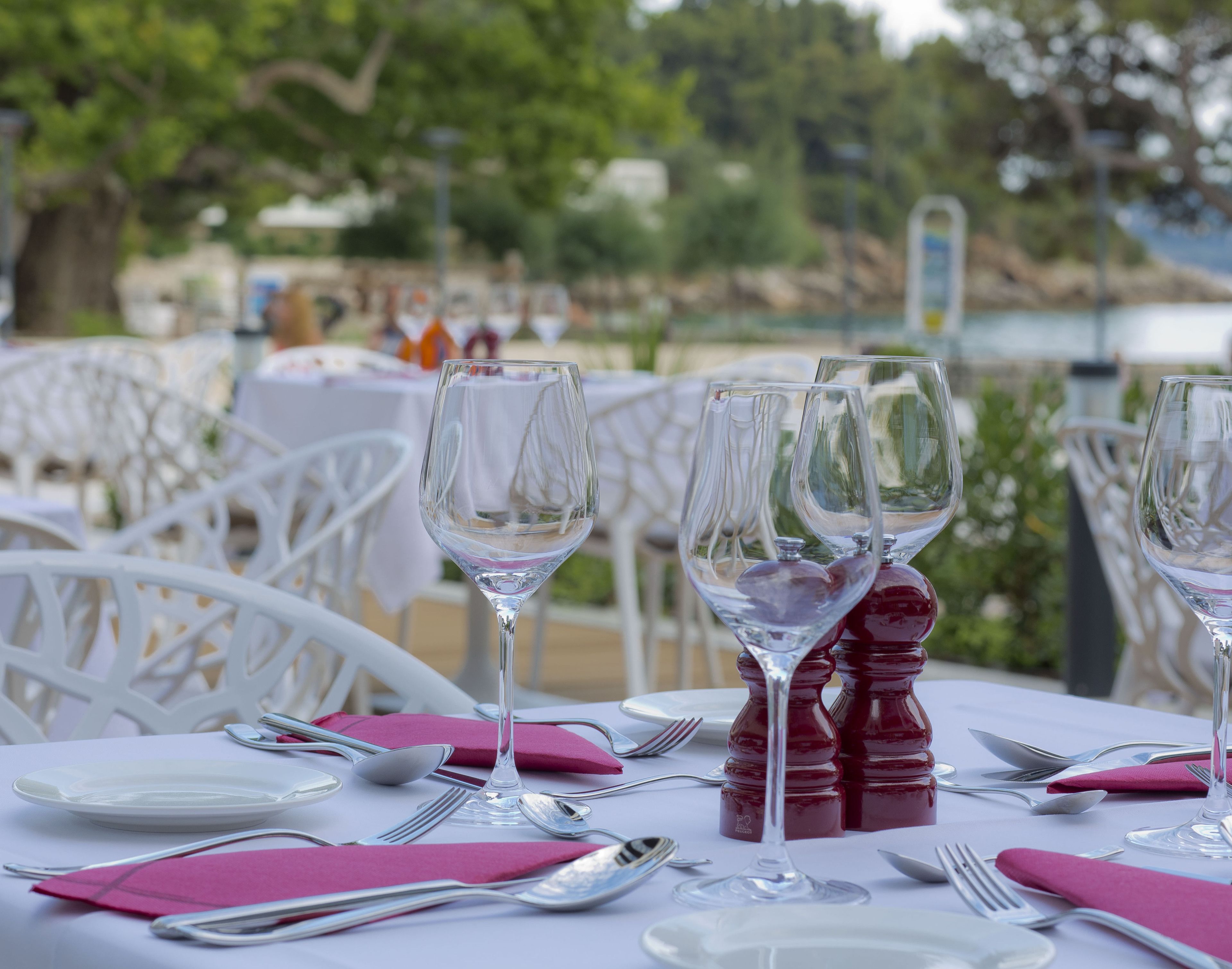 A table set for dining with white chairs and a view of the sea in the background.