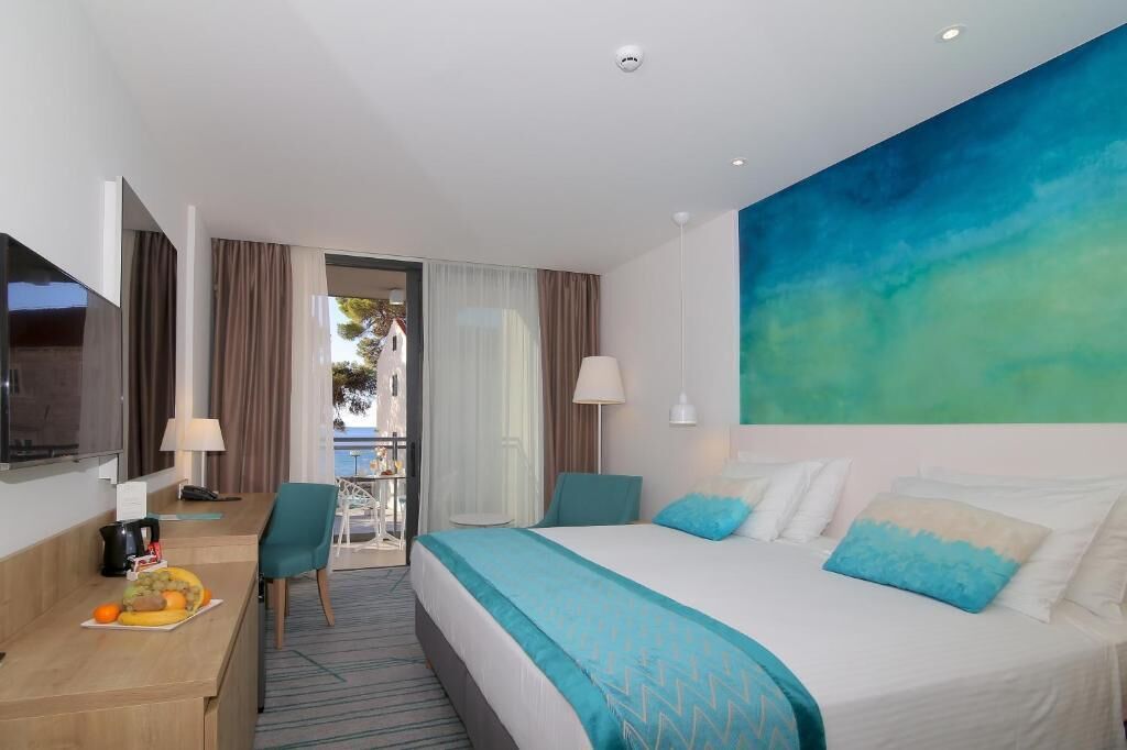 A hotel room with a bed, a desk with a chair, a TV, and a view of the outdoors.