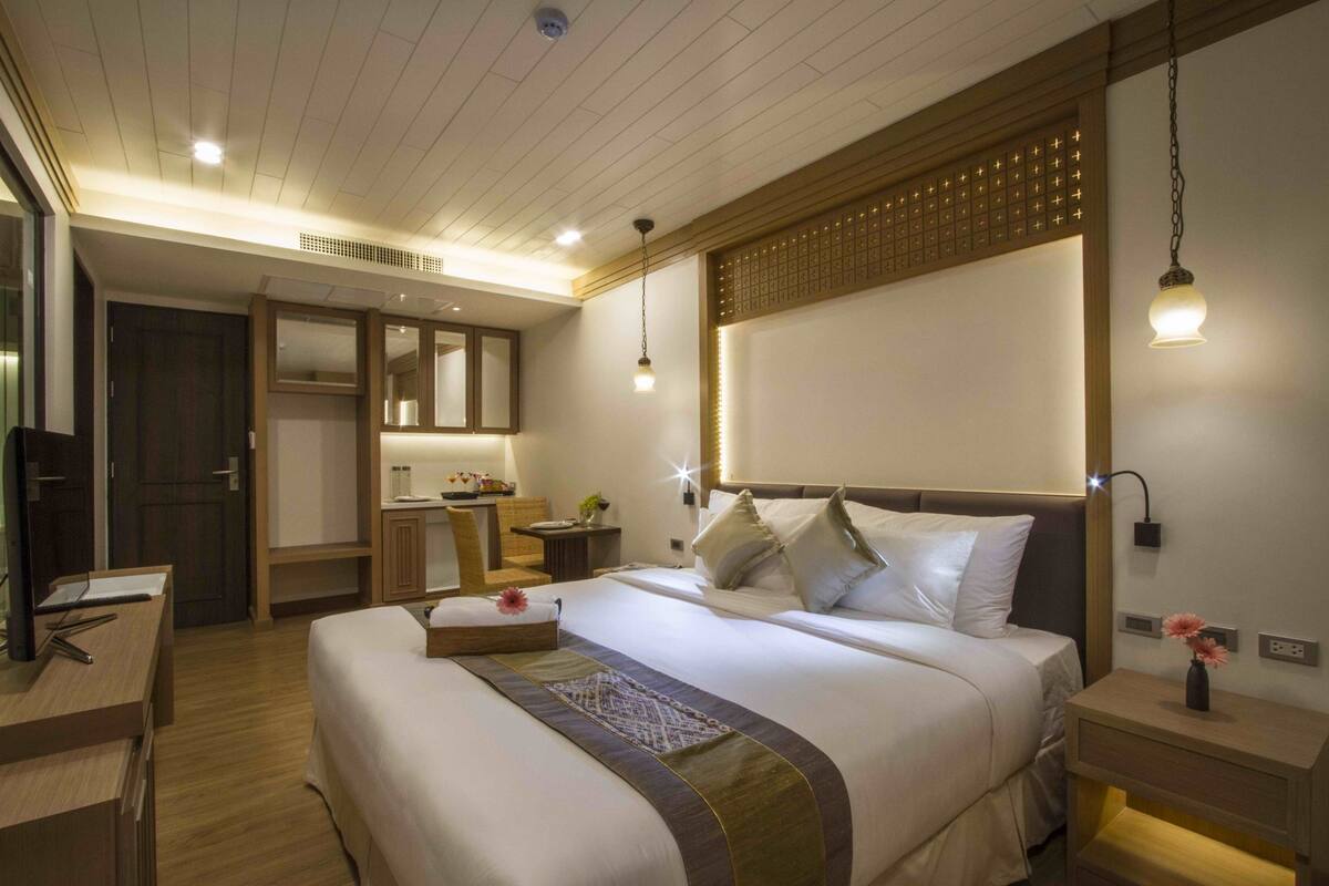 A hotel room with a large bed, bedside tables, a desk, a chair, a wardrobe, and a mirror.