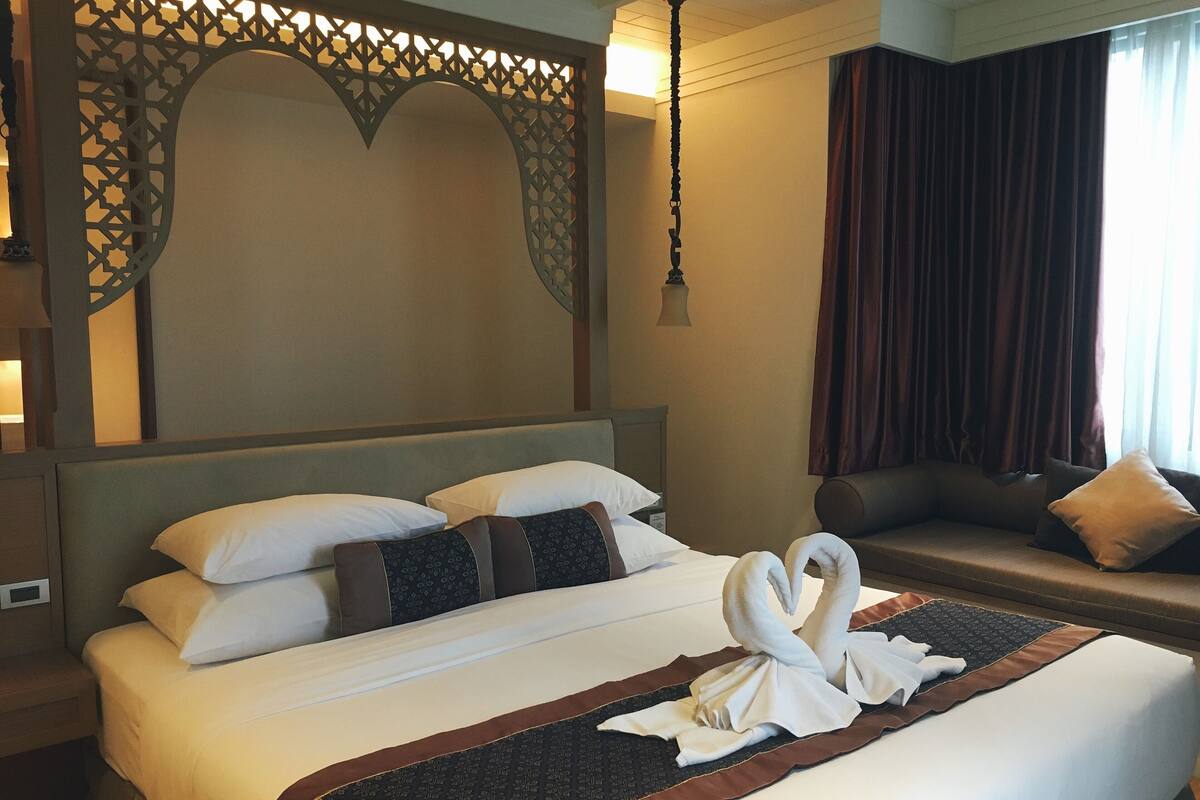 A hotel room with a neatly made bed, a sofa, and a decorative wall panel.
