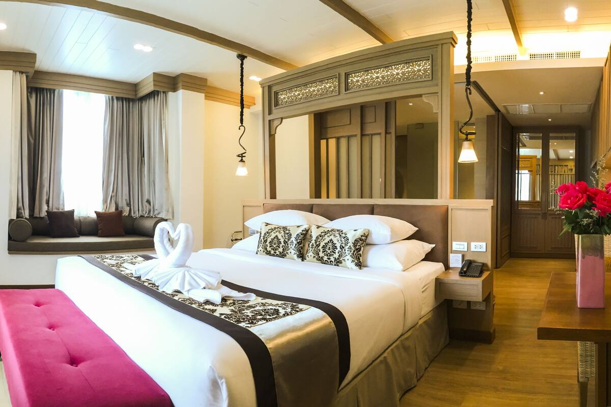 A hotel room with a large bed, a seating area, a dining table, and a mirror.