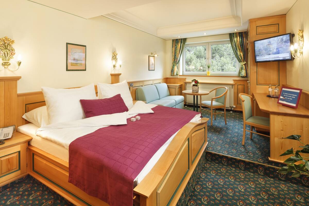 A hotel room with a bed, a desk, a chair, a TV, and a window with curtains.